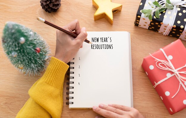 Женщина почерков новогоднюю резолюцию на бумаге для заметок в день нового года