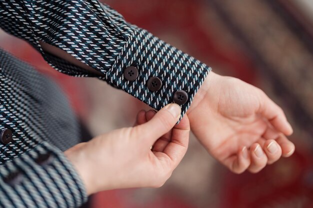 Woman hands buttoning the cuff on the shirt in a soft light Clothes details