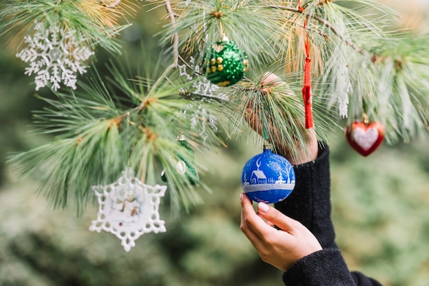 Woman hands hanging Christmas toys on twig in forest