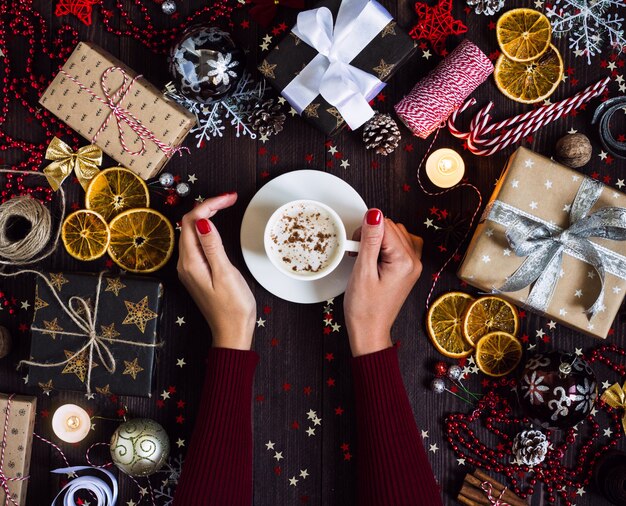 女性両手コーヒーカップを飲むクリスマスホリデーギフトボックスに飾られたお祝いテーブル