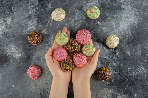 Mani della donna che tengono le ciambelle dolci variopinte con spruzza.