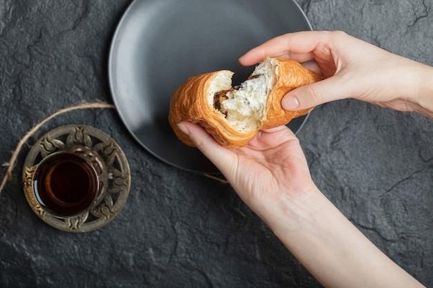 Woman hands holding a fresh croissant on a dark plate. 