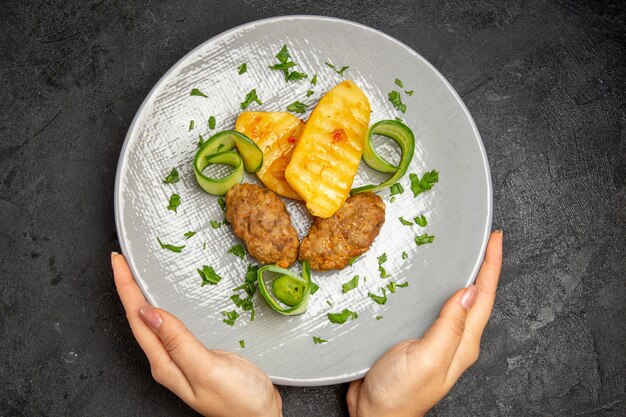 黒いテーブルの上の白いプレートにジャガイモと一緒にカツレツの食事とおいしい夕食を保持している女性の手