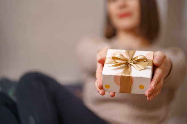 Woman hands holding wrapped white box with golden bow, focus on box