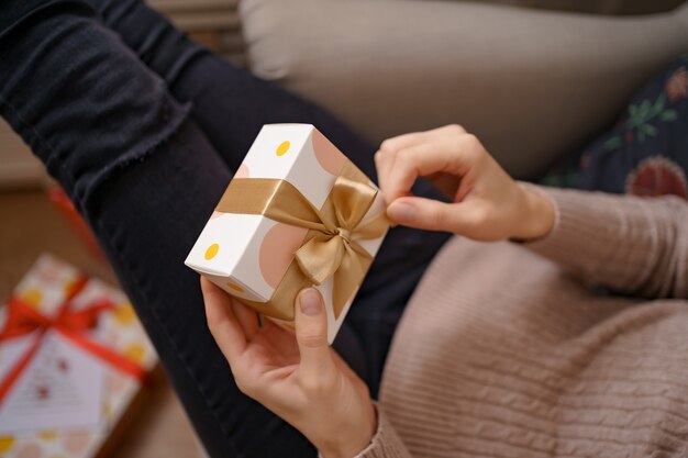 Woman hands holding wrapped white box with golden bow, focus on box