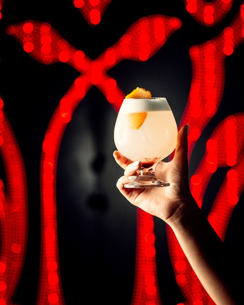 Женщина руки держит бокал коктейля с апельсиновой цедрой