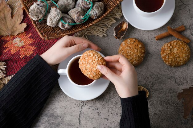 Woman hands putting oatmeal cookie in a cup of hot tea.