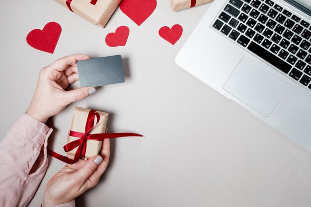 クレジットカードと白い背景の上のハートとコーヒーのラップトップギフトボックスと女性の手バレンタインデーオンラインショッピングコンセプト休日の背景上面図