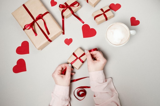 Woman hands with gift boxes red ribbon and hearts on white background Top view flat lay Valentine day