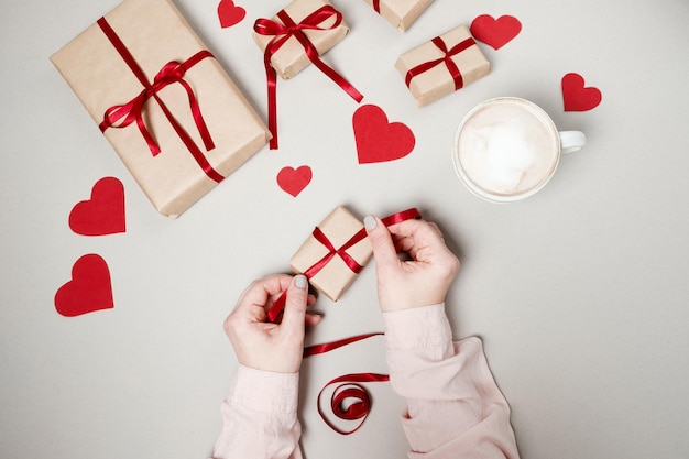 Женские руки с подарочными коробками, красной лентой и сердцами на белом фоне Вид сверху плоский лежал День святого Валентина