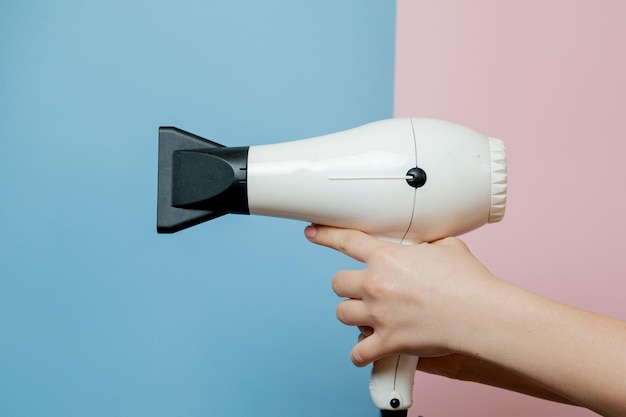 Woman hands with hair dryer on blue pink background Beauty concept