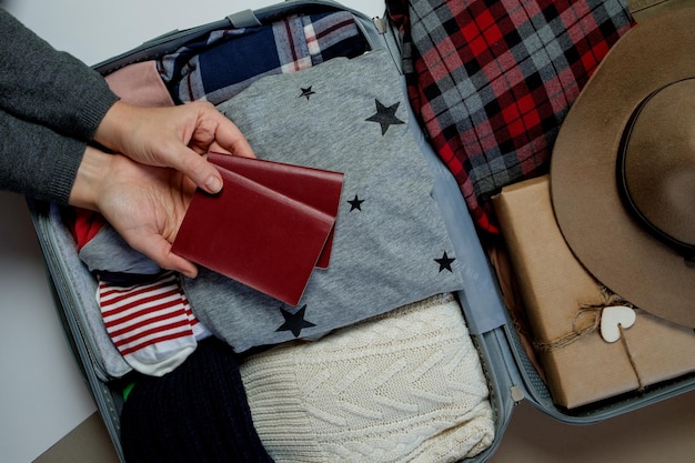 배경에 여권을 든 여자 손 겨울 방학 및 휴일 여행을 위해 포장된 열린 여행 가방 상위 뷰