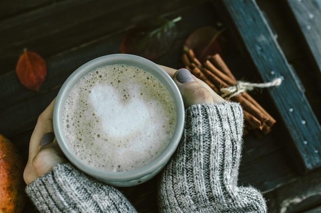 Free photo woman hands with spicy pumpkin latte on a wooden board with a sweater