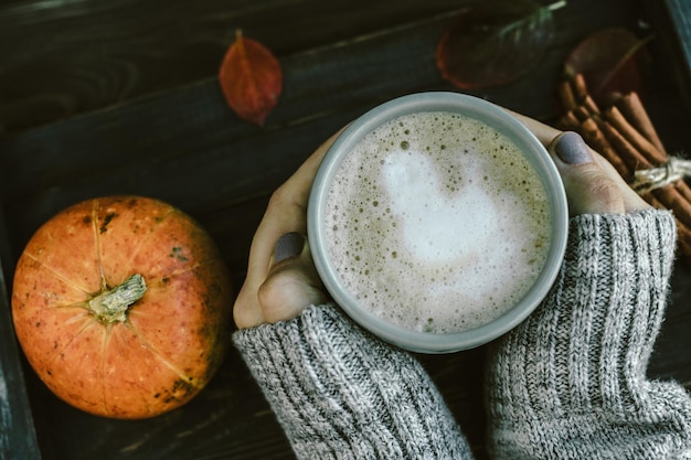 Woman Hands with Spicy pumpkin latte on a wooden board with a sweater