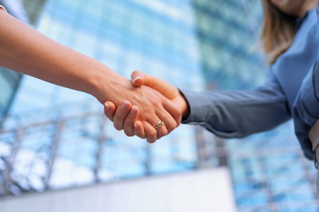 Woman handshaking outdoors over modern glass business building, close-up picture