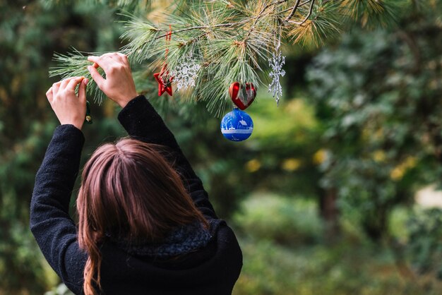 Woman hanging Christmas toys on twig in forest 