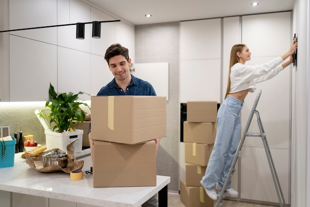 Woman hanging frame on the wall while her boyfriend is handling boxes