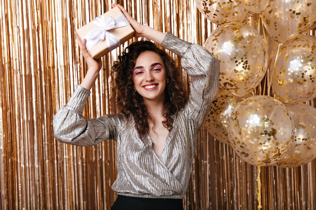 Free photo woman happily looks into camera and holds gift box