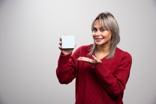 Woman happily showing memo pad on gray background.