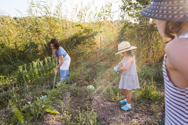 농장에서 그녀의 두 딸과 함께 야채를 수확하는 여자