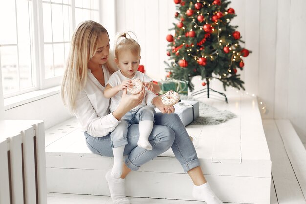 Woman has fun preparing for Christmas. Mother in a white shirt is playing with her daughter. Family is resting in a festive room.