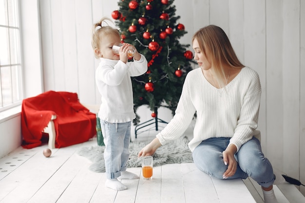 여자는 크리스마스를 준비하는 재미 있습니다. 딸과 함께 연주 흰색 스웨터에 어머니입니다. 가족은 축제 방에서 쉬고 있습니다.