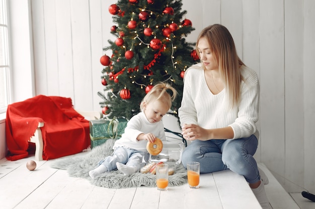 여자는 크리스마스를 준비하는 재미 있습니다. 딸과 함께 연주 흰색 스웨터에 어머니입니다. 가족은 축제 방에서 쉬고 있습니다.