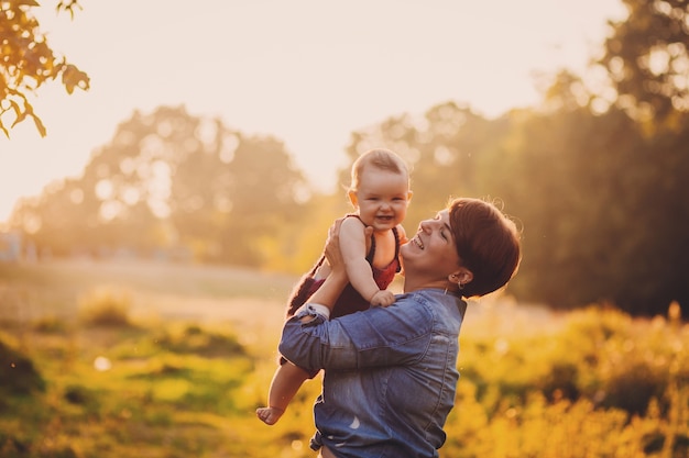 Woman has fun with little girl standing in the rays of golden sun 