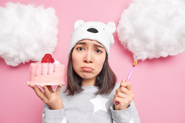 여자는 맛있는 달콤한 케이크를 먹고 싶은 유혹이 있지만 치아 문제가 두려워 칫솔을 들고