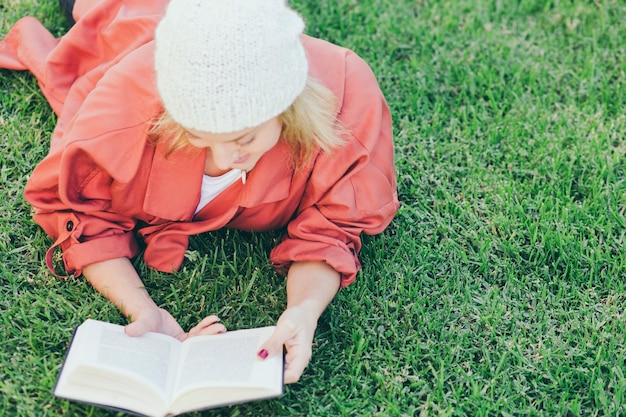 Woman in hat reading book on grass