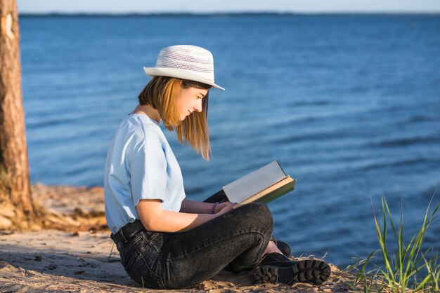 Woman in hat reading near sea
