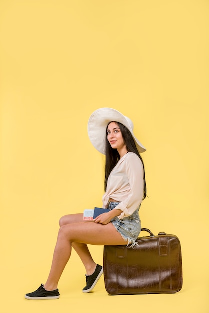 Woman in hat sitting on brown suitcase