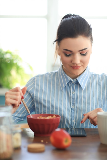 Donna che mangia prima colazione mentre chiacchiera con il suo telefono