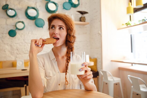 テーブルで牛乳とクッキーで朝食を持つ女性