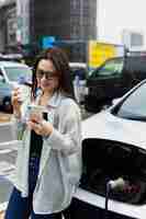 Free photo woman having a coffee break while her electric car is charging and using smartphone