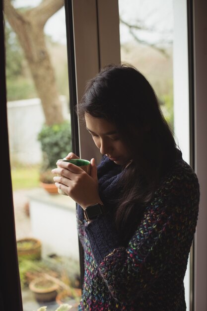 自宅の窓の近くでコーヒーを飲む女性