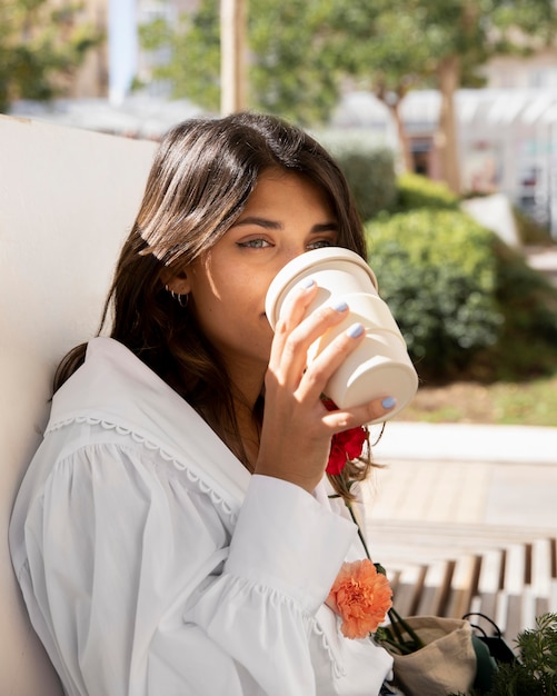 Женщина пьет кофе на открытом воздухе, держа цветы