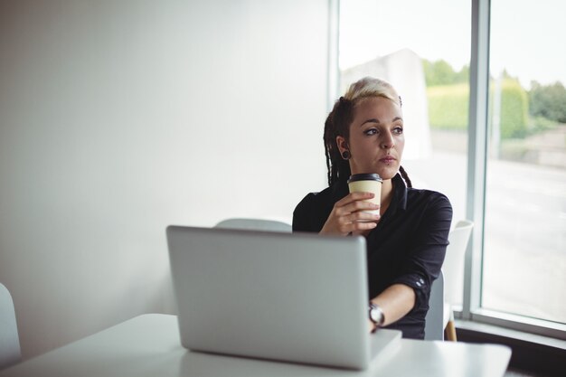 ラップトップを使用しながらコーヒーを飲んでいる女性