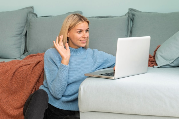 Woman having a video call at home on laptop and waving during the pandemic