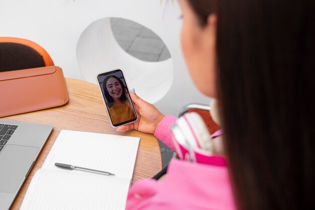 Woman having a videocall on smartphone while sitting at desk and taking notes