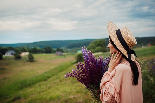 干し草の帽子の女は、フィールド上のラベンダーの花束とポーズ