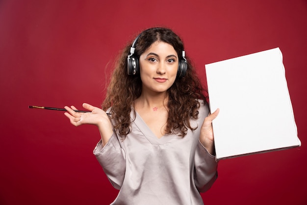 Woman in headphones posing with brush and canvas