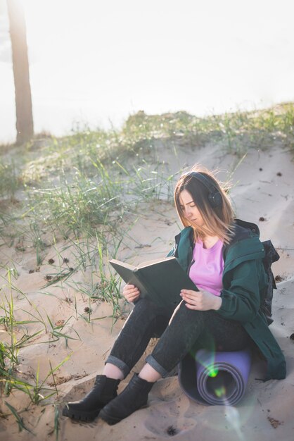 Woman in headphones reading book on beach