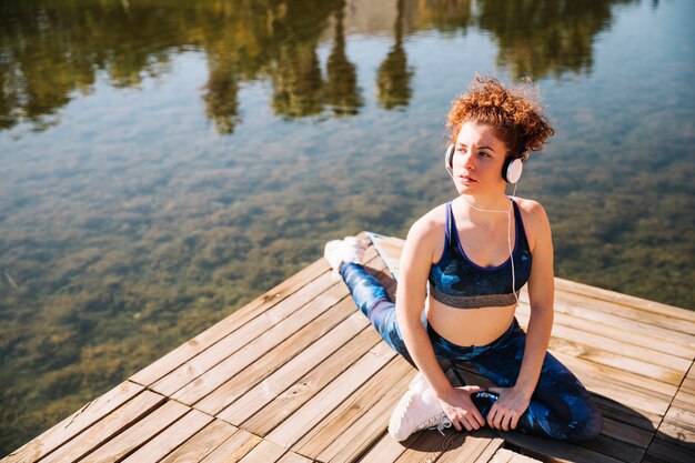 Woman in headphones stretching on pier