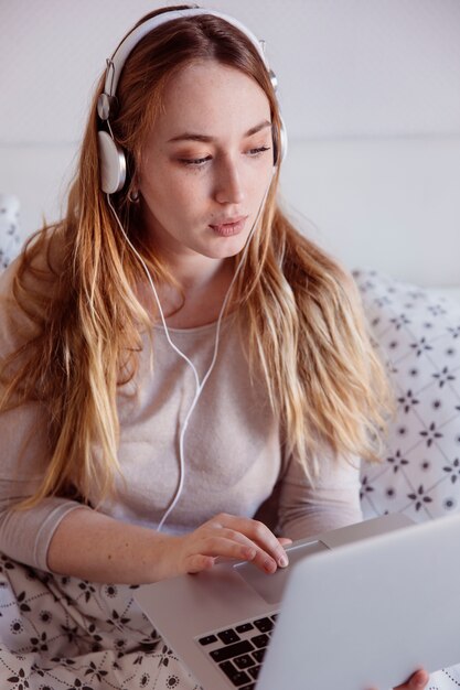 Woman in headphones using laptop in bed