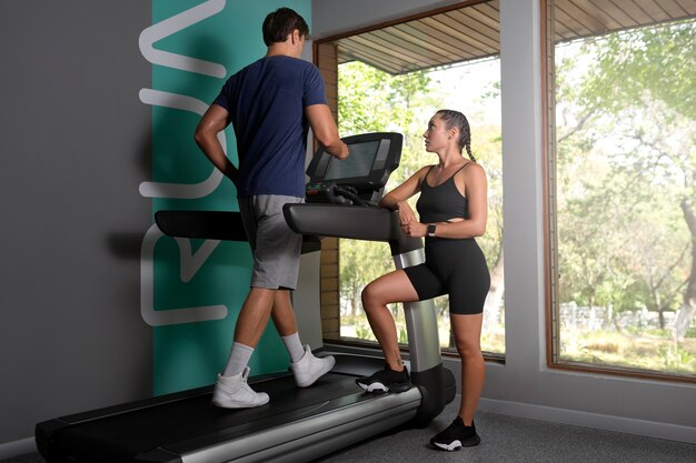 Woman helping man workout at gym full shot