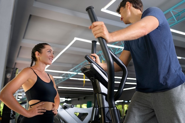 Foto gratuita donna che aiuta l'allenamento dell'uomo alla vista laterale della palestra