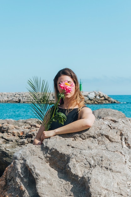 Woman hiding her face with beautiful flower standing near sea