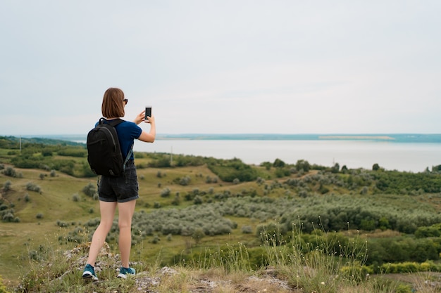 女性ハイカーは丘の頂上でスマートフォンで写真を撮影。