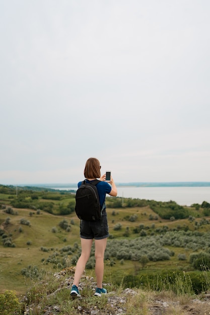 Hiker женщины принимая фото с умным телефоном на пик холма.